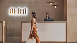 A woman walking past a reception desk with a sign that reads "ALBA". - HotelMOTEL Adelaide (Adelaide)