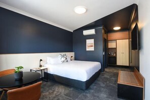 A hotel room with a bed, a desk, a chair, a small table with a plant, and a kitchenette area. - HotelMOTEL Adelaide (Adelaide)
