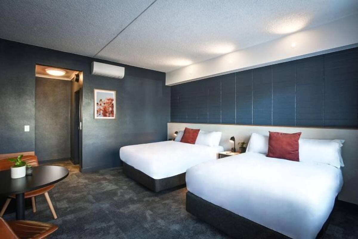 Hotellihuone, jossa on kaksi sänkyä, pieni pöytä ja tuoli.