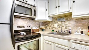 A kitchen with white cabinets, a microwave, an oven, a dishwasher, and a sink.
