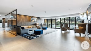 Una sala de estar moderna con un sofá, sillones y una mesa de centro. Hay una partición de vidrio con patrones geométricos y un ventanal con vistas al exterior.