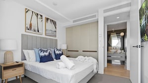 Una habitación de hotel moderna con una cama grande, una mesita de noche con lámpara, un armario y un baño visible a través de una puerta abierta.