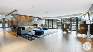 A modern living room with a sofa, armchairs, and a coffee table. There is a glass partition with geometric patterns and a large window offering a view of the outdoors.