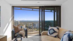 A modern living room with a sofa, a coffee table, and a view of a cityscape through large glass doors.