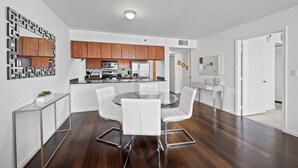 A modern kitchen with wooden cabinets, a central island, and a dining area with a round table and white chairs. - The Club 2020 Duplicate · Supber unit, centrally located with parking (Miami)