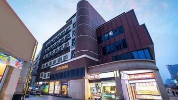A multi-story building with commercial spaces on the ground floor, including a brightly lit storefront and a restaurant.