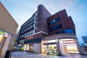 Un edificio de varios pisos con locales comerciales en la planta baja, incluyendo un escaparate bien iluminado y un restaurante.