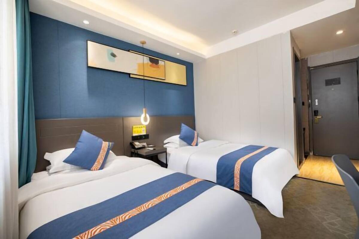 Quarto de hotel com duas camas, mesa de cabeceira, espelho e porta.