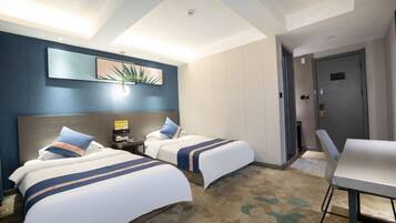 A hotel room with two beds, a desk, a chair, a nightstand, a wall-mounted lamp, and a door.