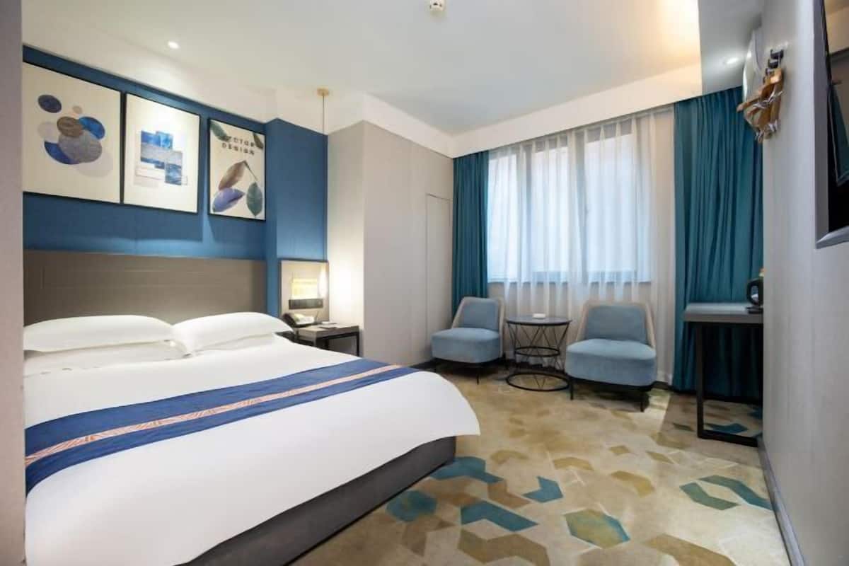 Habitación de hotel con cama, dos sillas, una mesita y una ventana con cortinas.