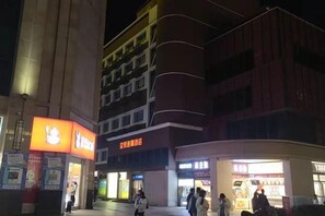 Un edificio con varias fachadas, que incluye un restaurante bien iluminado y una farmacia.