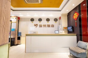 A hotel reception desk with a digital screen, a clock, and a red decorative element on the wall.