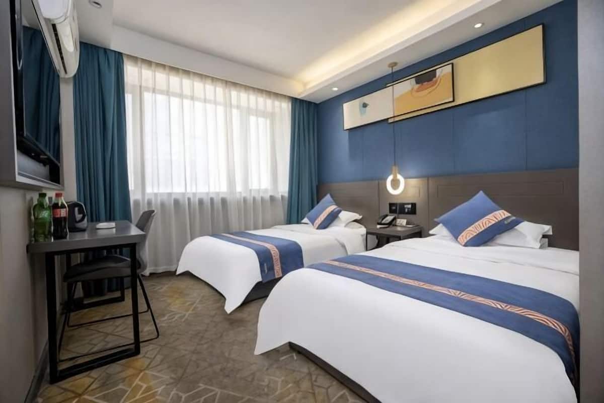 Habitación de hotel con dos camas, un escritorio, una silla, un televisor y una ventana con cortinas.