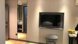 Ein modernes Hotelzimmer mit einem großen Spiegel, einem flachbildfernseher an der Wand, einem kleinen runden Tisch und einem sichtbaren Badezimmer im Hintergrund.