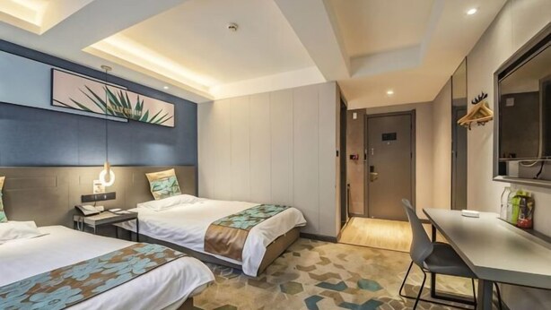 Ein Hotelzimmer mit zwei Betten, einem Schreibtisch, einem Stuhl, einem Spiegel und einer Tür.