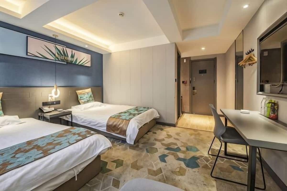Habitación de hotel con dos camas, un escritorio, una silla, un espejo y una puerta.