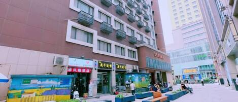 A multi-story building with a commercial ground floor, outdoor seating area with planters, and a clear sky.