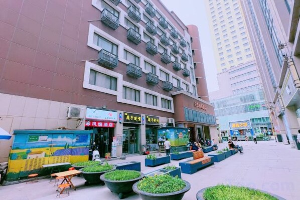 Un edificio de varios pisos con planta comercial, zona de estar al aire libre con macetas y cielo despejado.