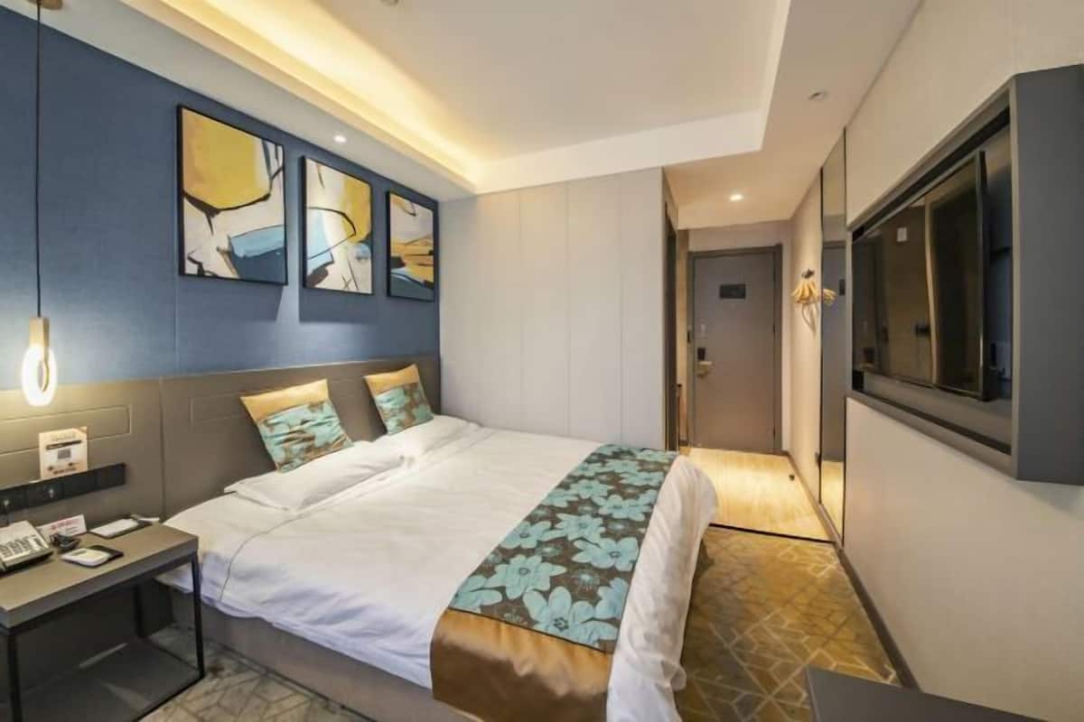 Una habitación de hotel moderna con una cama, una mesita de noche, una obra de arte y un ventanal grande.