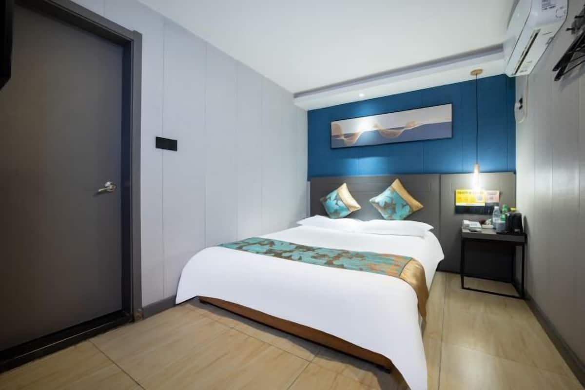 Habitación de hotel con cama, mesita de noche, aire acondicionado instalado en la pared y una puerta.