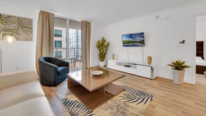 A modern living room with a sofa, a coffee table, a TV mounted on the wall, and a balcony with curtains. - The Club 1606 · Impressive Unit in the heart of Brickell W Parking (Miami)