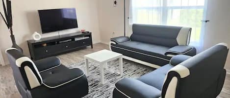 A living room with a black and white sofa set, a flat-screen TV, a coffee table, and a black entertainment unit.