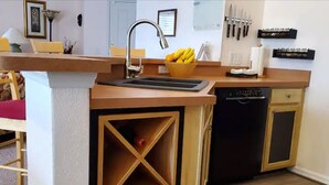 Eine Küche mit Holzarbeitsplatte, Spüle und Geschirrspüler. Auf der Arbeitsfläche steht eine Obstschale und an der Wand ist ein Messerblock angebracht.