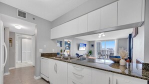 Una cocina moderna con gabinetes blancos, encimeras de granito y un amplio ventanal con vistas a la ciudad.
