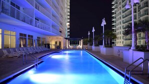 Una piscina con sillas de descanso, un área techada y un edificio con balcones.