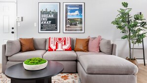 A modern living room with a grey sectional sofa, a round coffee table with a green plant, and two framed movie posters on the wall. - Little 5 Condo: King Beds | Ping-Pong | Garage (Bloomington)
