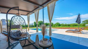 A covered outdoor seating area with a hanging chair, a lounge chair, and a table with a vase. - Amazing home in Jadreski with private swimming pool, can be inside or outside (Jadreski)