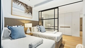 Une chambre d’hôtel avec deux lits, une grande fenêtre et un tableau représentant des palmiers.