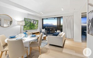 Relax in a spacious living room with a large flat-screen TV, dining area, and sofa seating, offering a panoramic view of the city and mountains.