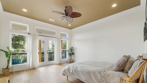 A spacious bedroom with a large bed, a ceiling fan, and a view of the outdoors through the windows.