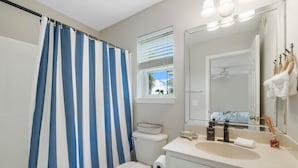 A bathroom with a striped shower curtain, a toilet, a sink with a mirror, and a window with blinds.