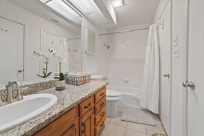 Une salle de bain moderne avec un comptoir en granit, un meuble-lavabo en bois, un grand lavabo, des toilettes, une baignoire et un rideau de douche.