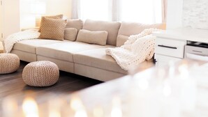 Ein modernes Wohnzimmer mit einem beigen Sofa, zwei runden Hocker, einem Deckenventilator und einem großen Fenster mit Vorhängen.