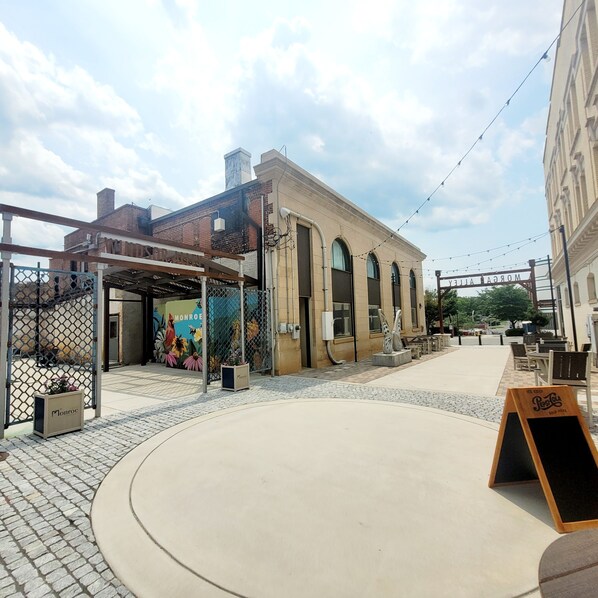 An outdoor seating area with tables and chairs, a mural on the building, and a Pepsi sign.