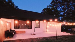 Een huis met een overdekte patio, een houten terras en lichtjes.