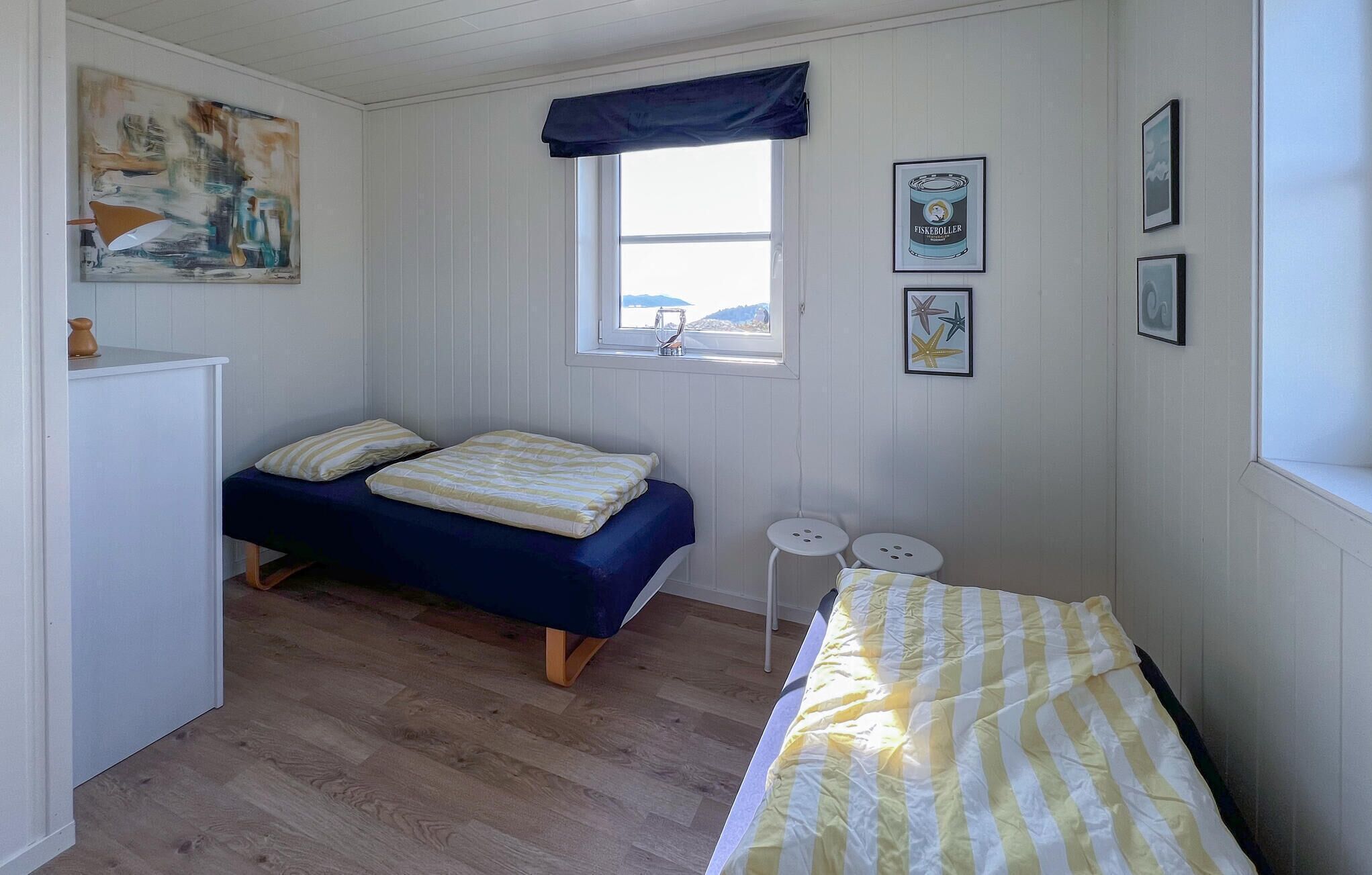 A small, cozy room with two single beds, a window with a view, and a painting on the wall.