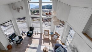 A spacious room with a large bay window offering a view of a forested area and mountains. There are two chairs and a sofa arranged on a wooden deck. - Amazing home in Lyngdal with WiFi (Lyngdal)