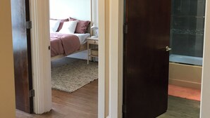 Hotellihuone, jossa on puulattia, valkoinen päätyosaan varustettu sänky, yöpöytä ja pieni työpöytä.