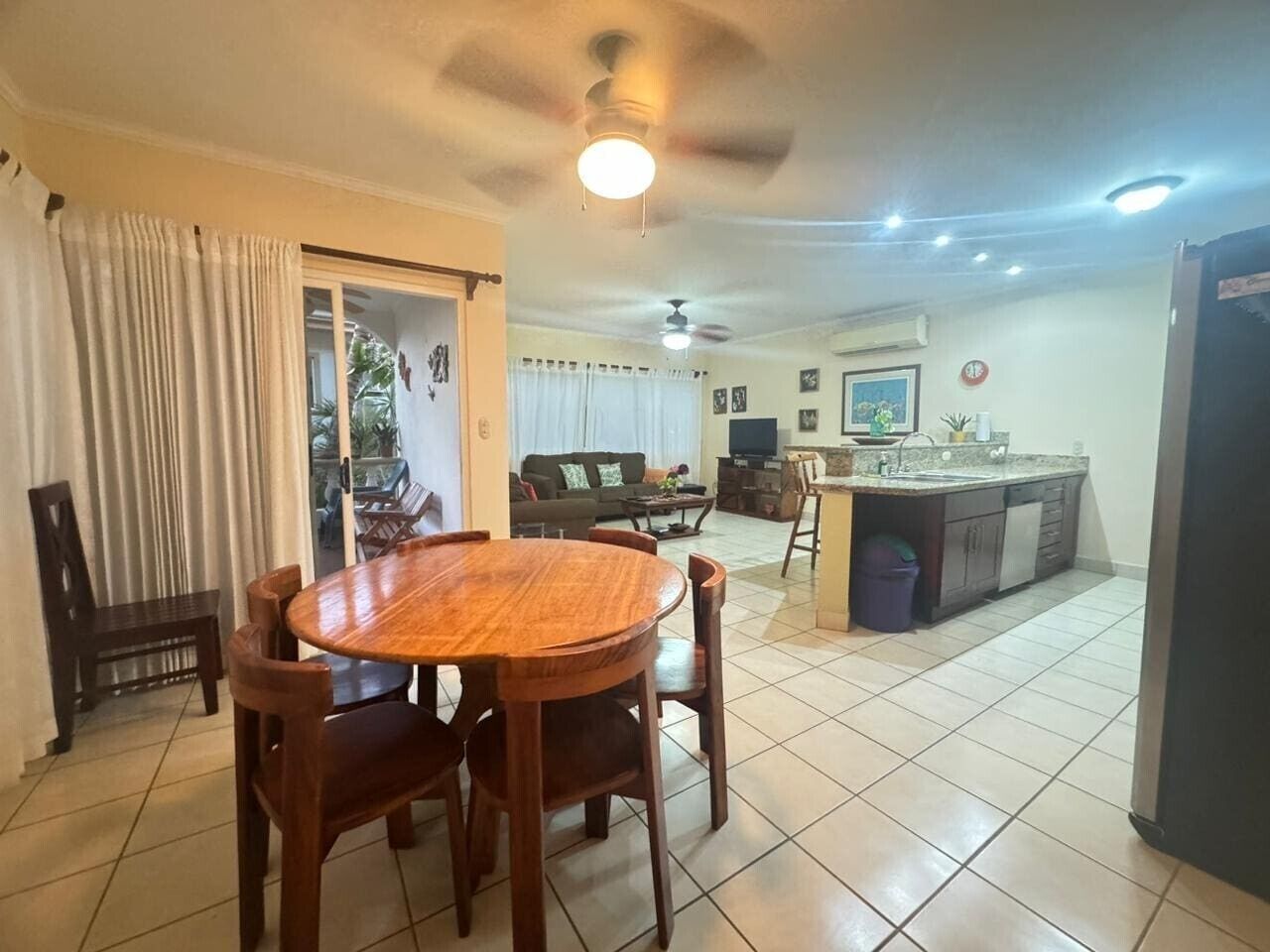 Un comedor con mesa y sillas de madera, una cocina con fregadero y encimera, y una sala de estar con sofá y mesa de centro.