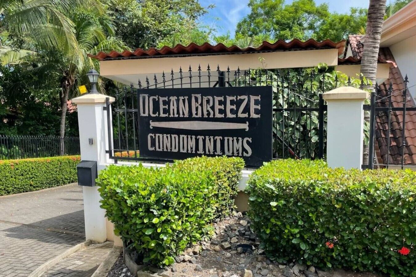 En skylt för Ocean Breeze Condominiums, med en grind vid ingången och frodig grönska.