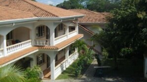 Edifici de dues plantes amb una piscina, envoltat de vegetació.