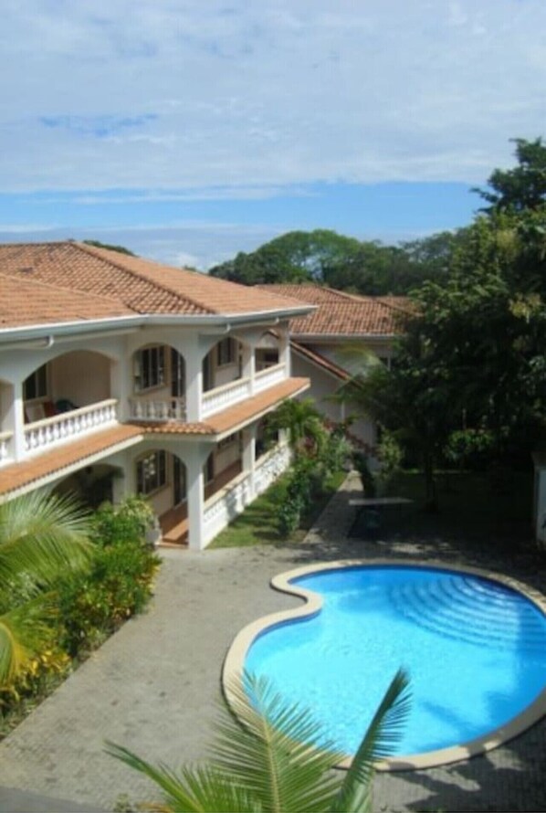 Um edifício de dois andares com piscina, cercado por vegetação.