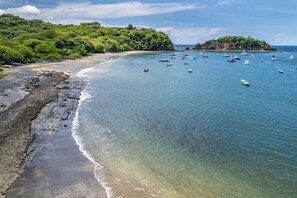 A coastal beach with boats, clear water, and lush greenery.