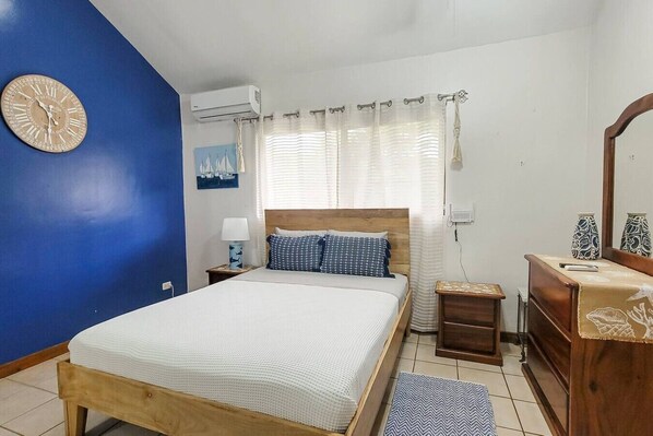A bedroom with a bed, bedside tables, a dresser, a clock, and a window with curtains.