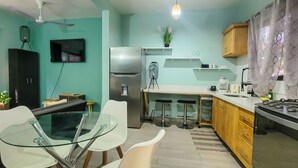 Una cocina moderna con zona de comedor, que incluye una mesa y sillas de vidrio, un refrigerador, una estufa y un ventilador de techo.