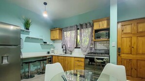 Una cocina compacta equipada con refrigerador, microondas, estufa y una mesa de vidrio con sillas.